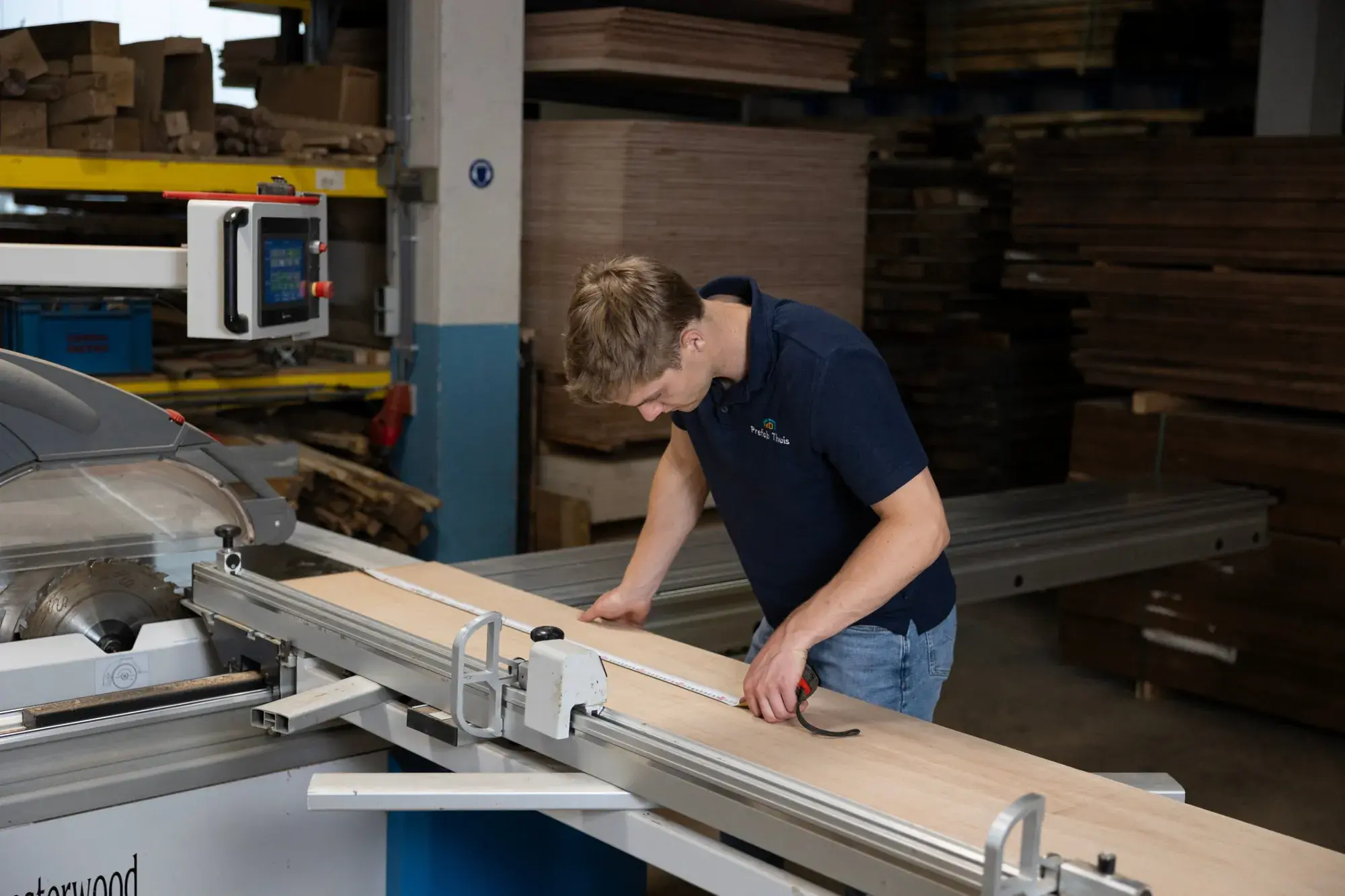 Een van de oprichters neemt de maat op een plaat op de formaatzaag in de werkplaats