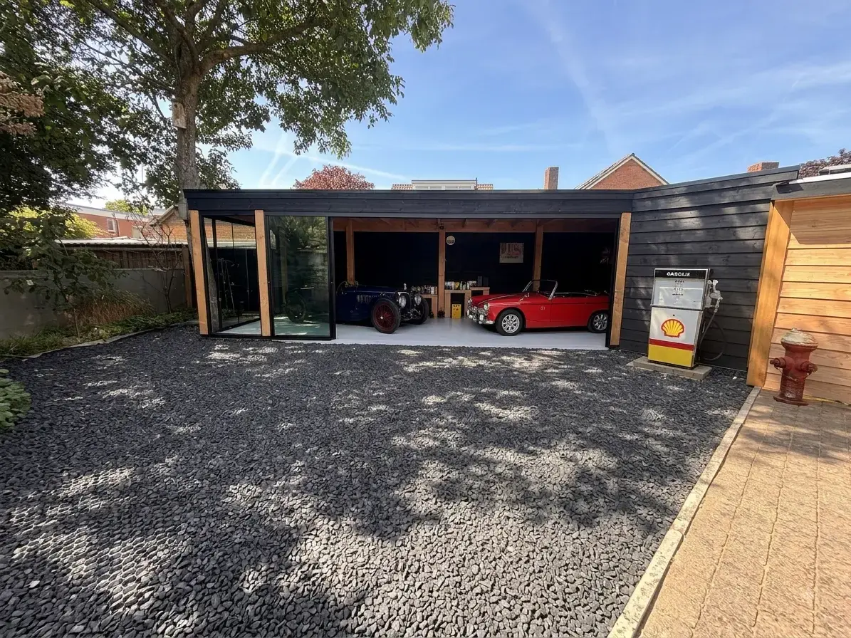 Maatwerk carport met zwarte houten gevel, douglas staanders en glazen wand, met twee oldtimers op een lichte betonvloer in Beneden-Leeuwen