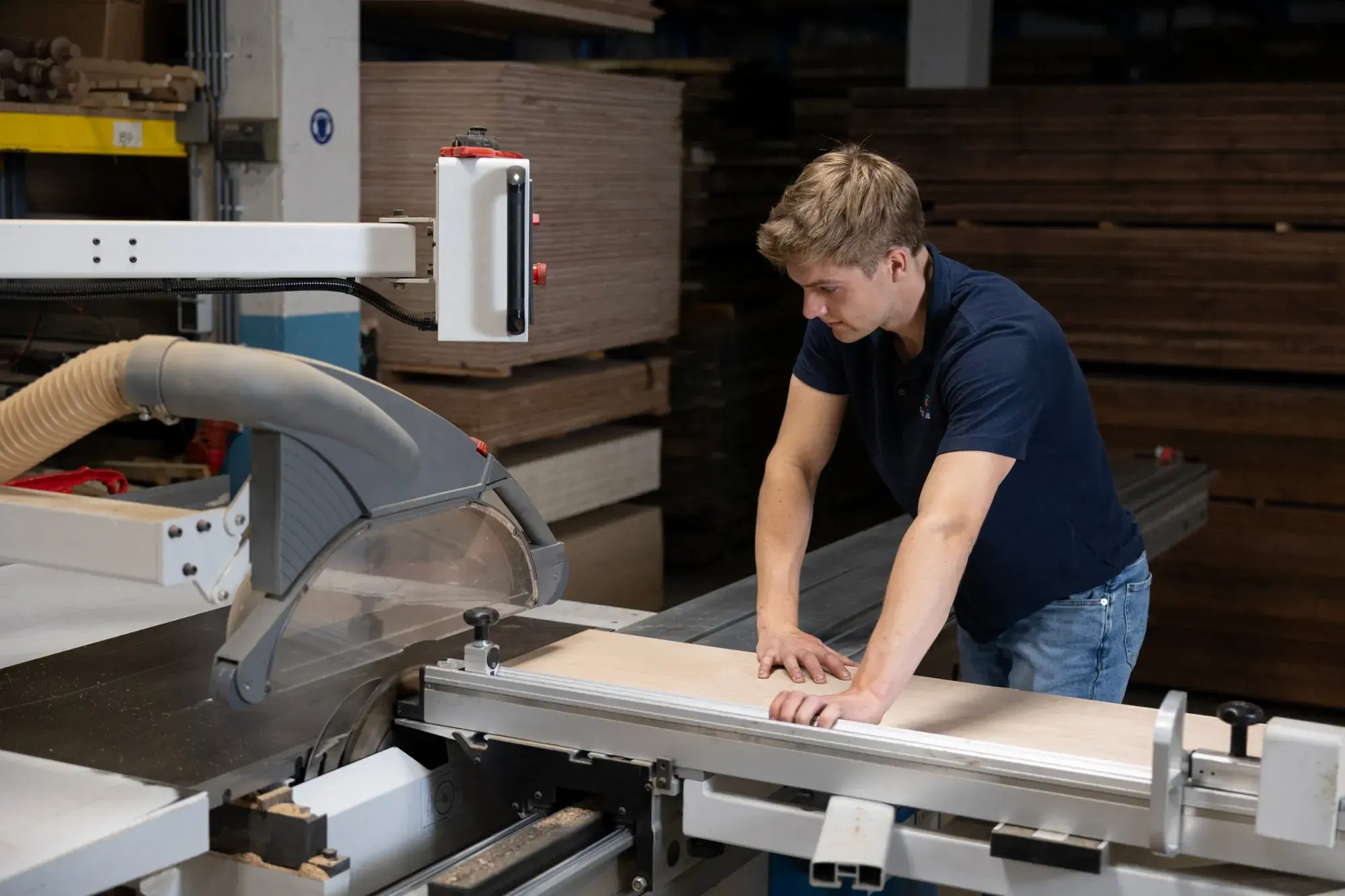 Een van de oprichters van Prefab Thuis zaagt een plaat op maat op de formaatzaag, met stapels hout op de achtergrond
